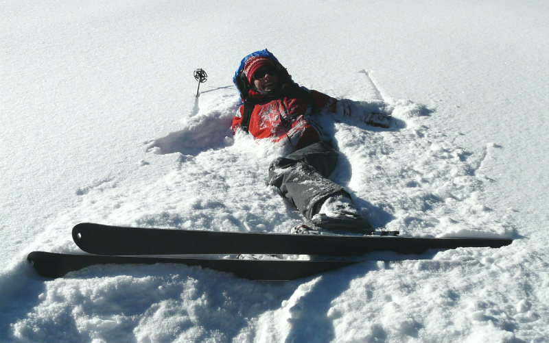woman lying in snow wearing skis