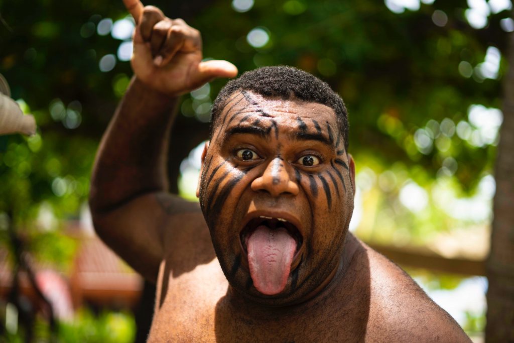 A Fijian man with his face painted and his tongue sticking out.